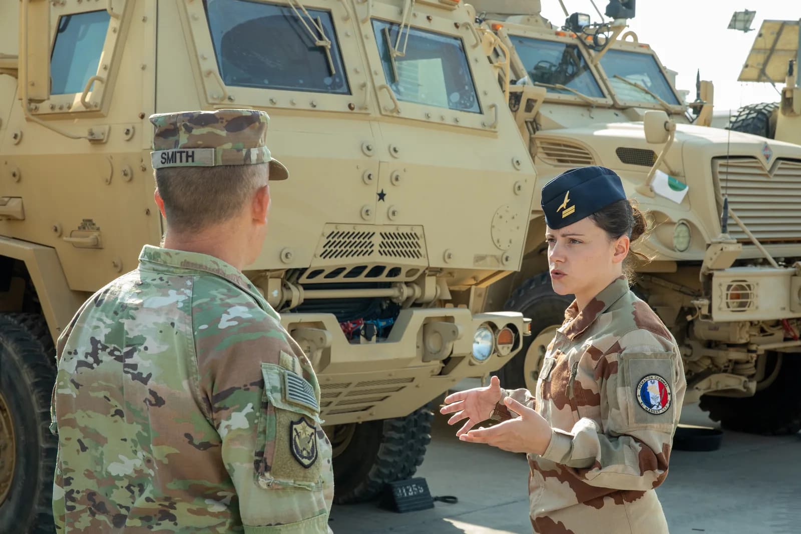 Aviatrice française échangeant avec un sous-officier américain devant des blindés MRAP au Koweït
