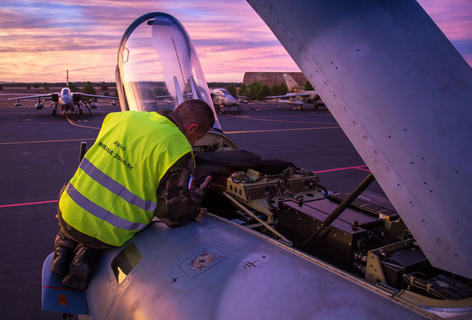 Avionicien de l'armée de l'air penché dans la baie avionique d'un Mirage 2000-5F au lever du jour