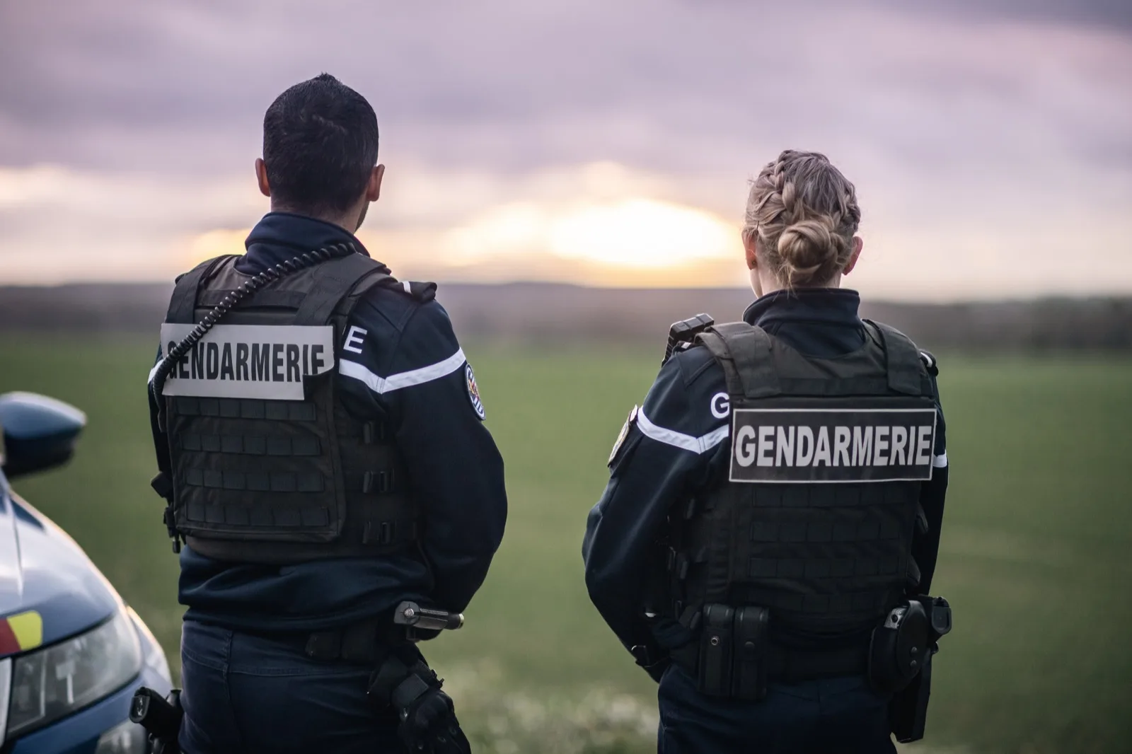 Deux gendarmes départementaux, une femme et un homme, face au coucher de soleil près de leur véhicule